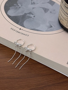 Close-up of silver bow tassel ear cuff clips on a decorative book with elegant lighting