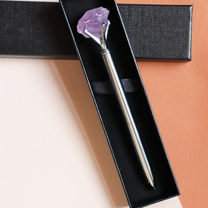Close-up of silver metal pen with raw purple crystal in a black gift box packaging