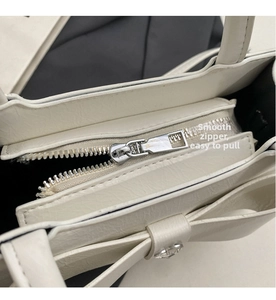 Detail of white crossbody bag with metal zipper, large bow, and rhinestone accents