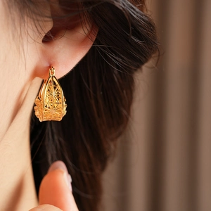 Macro shot of gold hollow geometric earrings on ear with high metallic luster detail