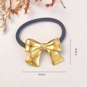 Detail of a black elastic hair tie with a 4.3cm golden metal bow on white background