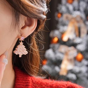 Close-up of pink zircon Christmas tree earrings with star charm on model wearing red sweater
