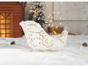 Close-up of a white plush Christmas sleigh decor with golden branch patterns and white metal legs