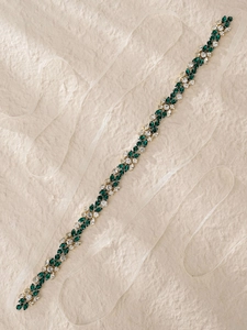 Detailed close-up of emerald and crystal bridal belt with white satin ribbons on textured paper