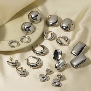 Polished silver hollow hoop earrings and geometric studs on a silk beige background