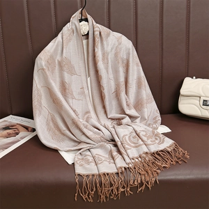 Dettaglio di una sciarpa pashmina beige con motivo paisley e nappe su pelle marrone