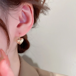 Close-up of a model wearing a gold heart-shaped earring with a textured molten metal finish