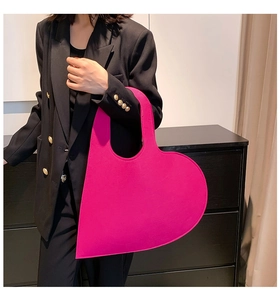 Detail view of large magenta heart-shaped felt handbag styled with a black blazer