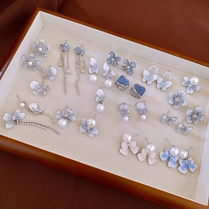 Detailed overhead view of blue floral and pearl earrings in a velvet jewelry tray