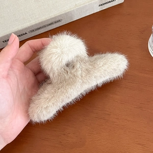 Détail d'une grande pince à cheveux en fausse fourrure beige montrant la texture douce