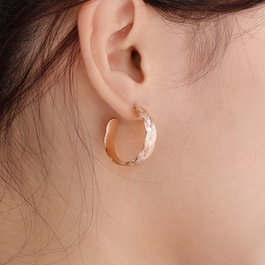 Close-up of rose gold stainless steel hoop earrings with woven texture on ear lobe