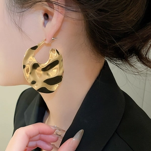 Close-up of oversized gold geometric earrings with black spotted texture on a model