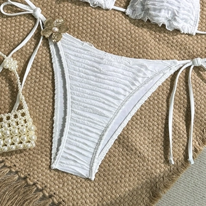 Detail of white smocked bikini bottoms with gold flower accent and pearl center