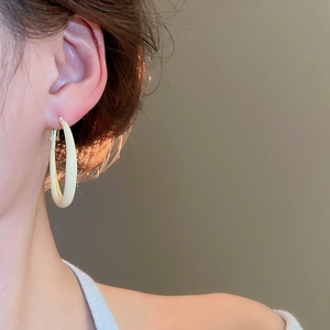 Detail of cream oval hoop earring worn by model with minimalist polished finish