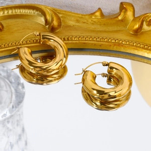 Chunky gold C-shaped twisted hoop earrings reflecting on a mirror with vintage frame