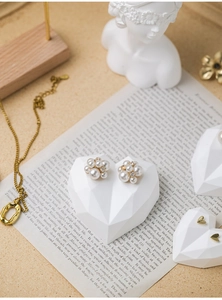 Close-up of pearl earrings and gold necklace on heart display stand with artistic props