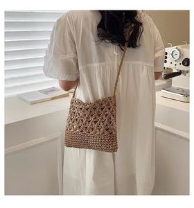 Detail of hand-woven straw crossbody bag with hollow floral pattern on white dress