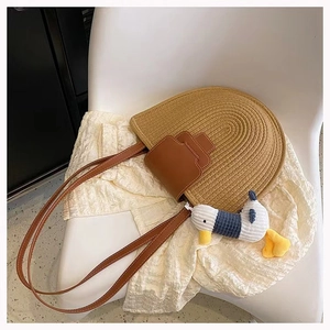 Detail of semi-circular straw bag with brown PU leather flap and small duck charm