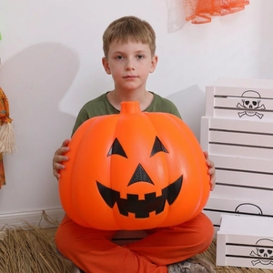 Large Halloween Jack-O-Lantern pumpkin prop held by a child on a rustic hay background
