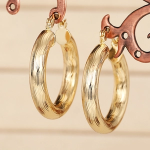 Elegante goldene Creolen mit unregelmäßiger Wellentextur auf vintage Schmuckständer