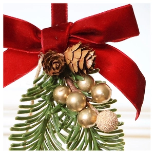 Detail of Christmas ornament with velvet red bow, pine cone, and golden ball on pine needles