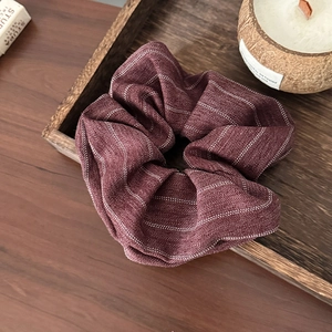 Detail of burgundy striped fabric scrunchie on wood tray with aromatic candle