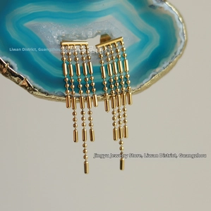Close-up of long gold tassel earrings with bead chains on blue agate slice