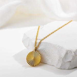 Detailed view of an 18k gold plated sunburst pendant on a white textured background
