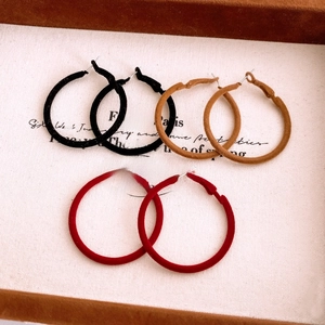 Detail of three pairs of large velvet-coated hoop earrings in black, brown, and red