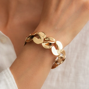 Detailed close-up of golden S-shaped twisted metal link bracelet on a model's wrist