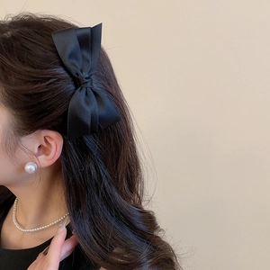 Barrette nœud double en satin noir sur cheveux longs bouclés pour un look rétro chic