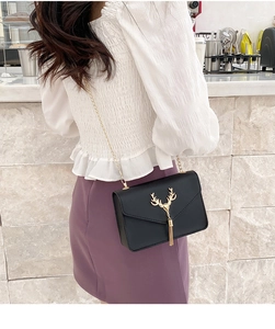 Detailed view of a black crossbody bag featuring a golden deer head and metal tassels