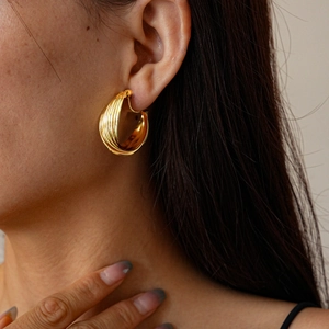 Close-up of golden multi-layer twisted metal clip-on earrings on a female model's ear
