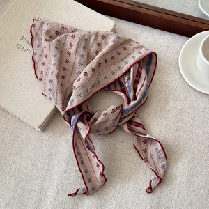 Close-up of beige floral striped scarf with red wavy edges on a linen background