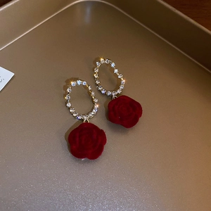 Detail of red velvet rose earrings with gold crystal oval hoops on a metal tray