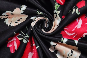 Dettaglio macro di tessuto satinato nero con stampa floreale rossa e rosa e seta liscia
