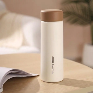 Detail view of a 400mL matte cream vacuum flask with a dark brown lid on a wooden table