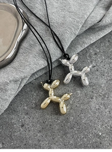 Detailed view of silver and gold balloon dog pendants on black cords over stone background