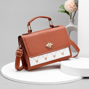 Brown and white bee crossbody bag with orange heart embroidery on an elegant display