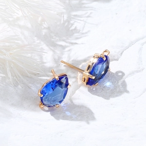 Blue teardrop zircon earrings with 14k gold plated setting on a white textured surface