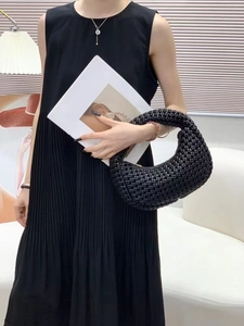 Detail of a black woven crescent handbag paired with a pleated dress and necklace
