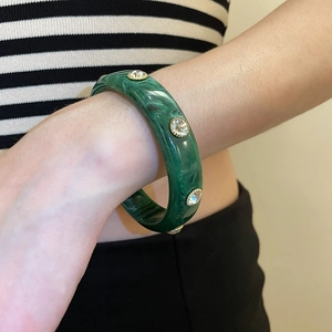 Detail of green acrylic bangle with malachite pattern and gold-tone rhinestone settings