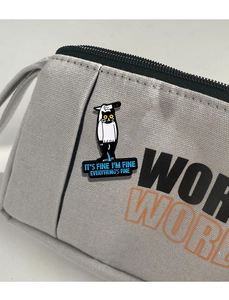 Close-up of a cartoon cat enamel pin with IT'S FINE text on a canvas pencil case
