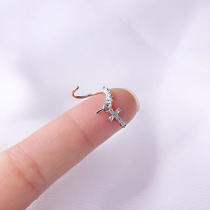 Macro shot of silver 20G nose ring featuring a small cross pendant with clear zircons