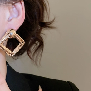 Close-up of geometric gold layered square earrings worn to show fashion texture