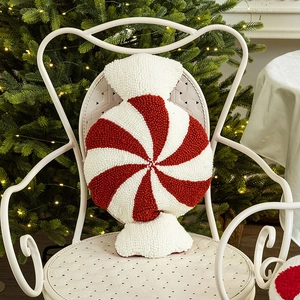 Red and white candy cane throw pillow on a chair with festive Christmas tree background