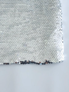 Dettaglio di paillettes circolari argento scintillanti su una gonna con spacco