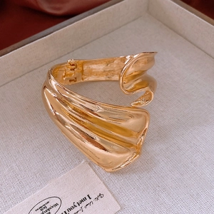 Detailed view of wide gold cuff bracelet featuring modern liquid metal pleated texture