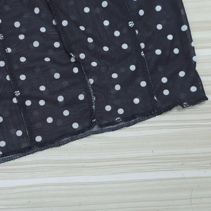 Detailed close-up of sheer black mesh fabric with white polka dots and wavy hem finish