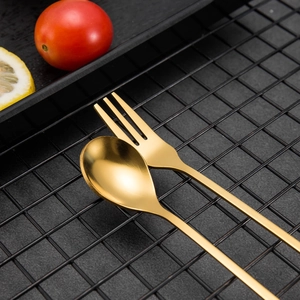 Detail shot of golden leaf dessert spoon and fork set on a black metal grid background